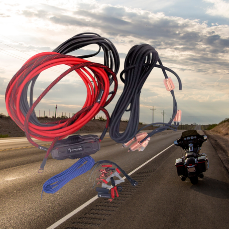 Jumper cables, wires, and clamps are shown over a deserted highway with a motorcycle parked on the roadside under a cloudy sky.