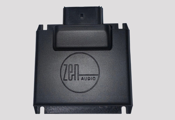 A black rectangular device labeled zen AUDIO in a circle, with a connector at the top, designed for audio equipment. The background is plain light gray.