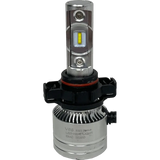 Close-up of a LUMI Stage 2 5202 LED Headlight Bulb by Lumi, featuring a silver body with cooling fins, a black plastic base, and a yellow CSP chip. The label reads V8S LED Headlight EMC 2020D. This high-performance bulb is equipped with advanced CSP chips that provide bright 6000K illumination. The background is plain white.