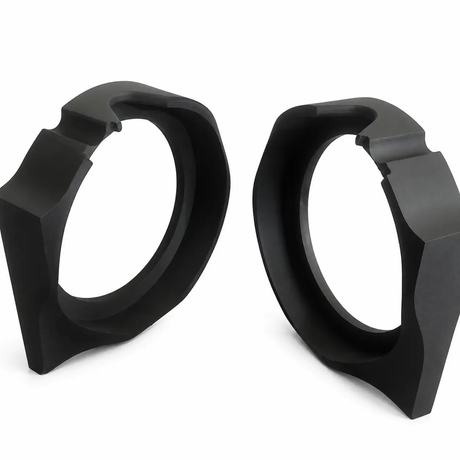 Two black, geometric, ring-shaped objects with angular edges—Nagy’s Customs Harley Davidson 8″ Sub / MidBass Mounts (1998-Present)—are positioned upright on a white surface, facing each other.