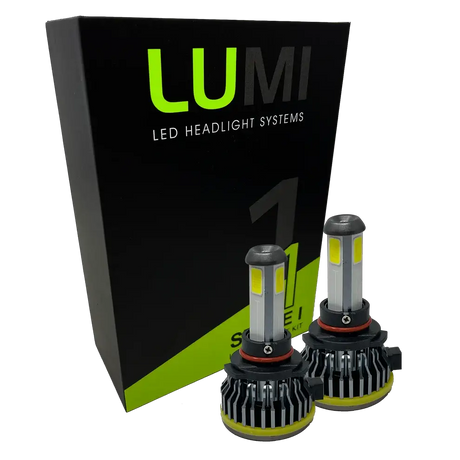 Two LUMI Stage 1 9005 LED Headlight Bulbs are displayed in front of a black and green Lumi LED Headlight Systems box. Featuring silver tops, black bases, and yellow accents, these bulbs are engineered with integrated LED CANBUS technology to deliver a bright 6000K white light for superior visibility.